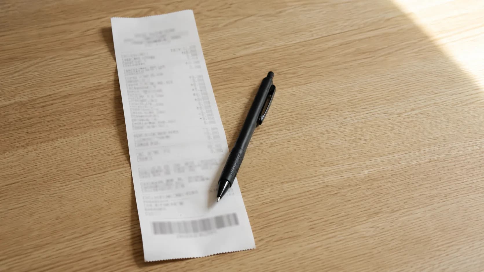 Representative illustration of a thermal receipt on a pale wooden counter beside a black ballpoint pen, depicting a manager-escalated receipt with a visible timestamp area and no readable text.