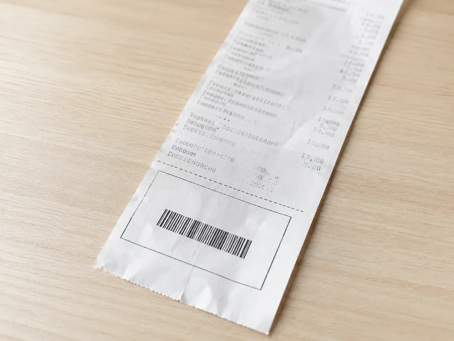 Close-up of a thermal paper receipt with a barcode and coupon section on a light wood table, illustrating a store-issued coupon received after an Amazon return drop-off.