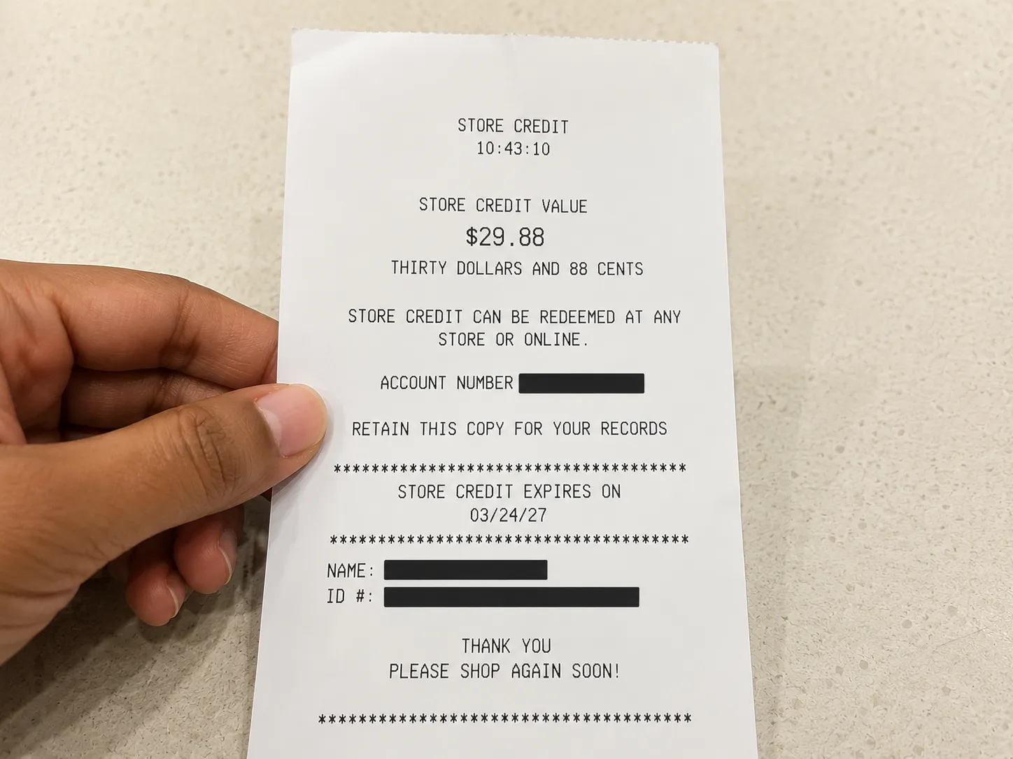 Hand holding a store credit slip from a no-receipt return, showing the gift card value while the ID number and other personal details are redacted.