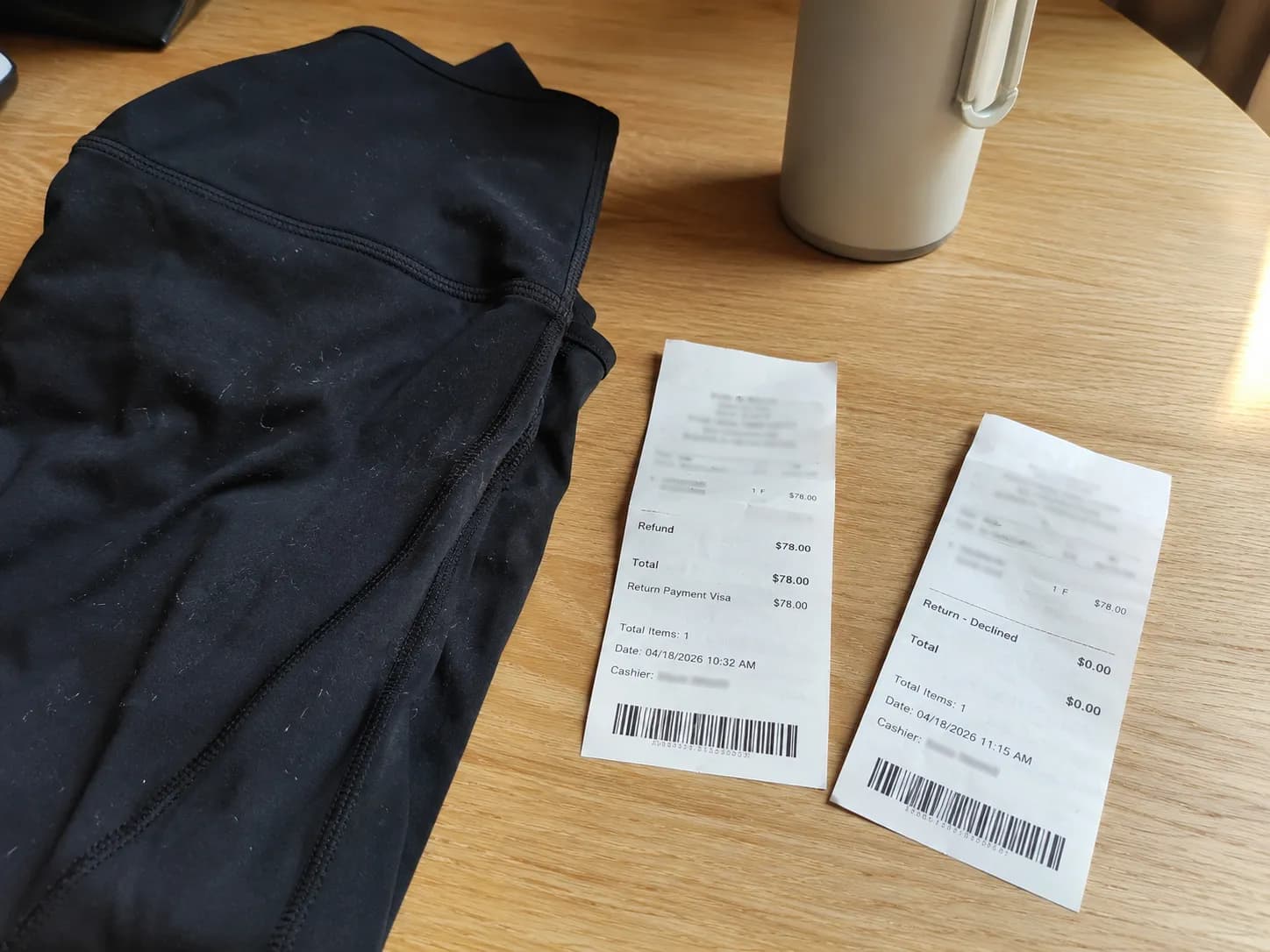 Close overhead photo of a worn pair of folded black athletic leggings beside two retail receipts, one showing an accepted refund and the other a declined return, illustrating a comparison of athletic