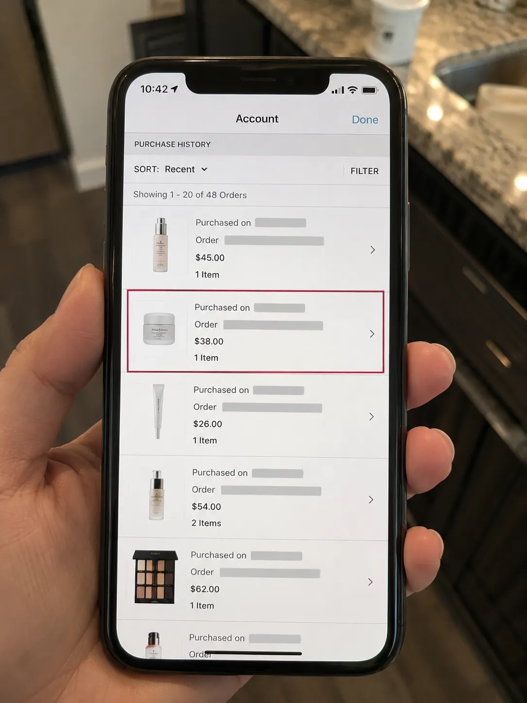 Smartphone displaying a loyalty account purchase history with personal details redacted and one order highlighted, used as proof of purchase in warm indoor lighting.