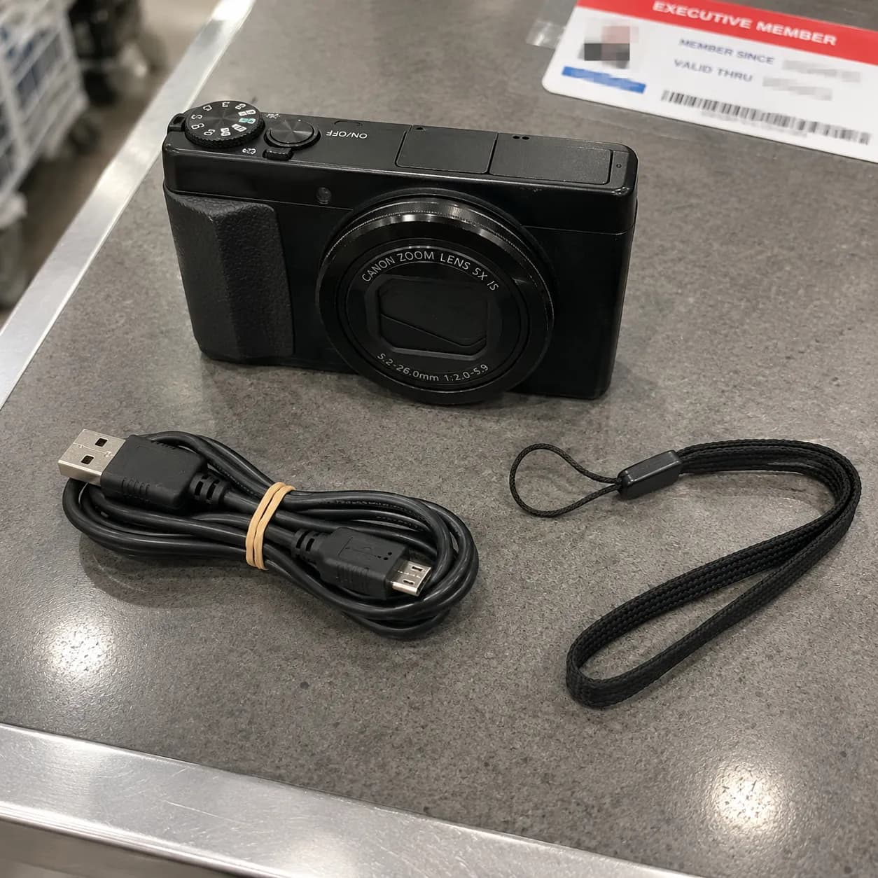 Used camera with charging cable and wrist strap on a Costco returns counter, showing accessories matter more than the box.