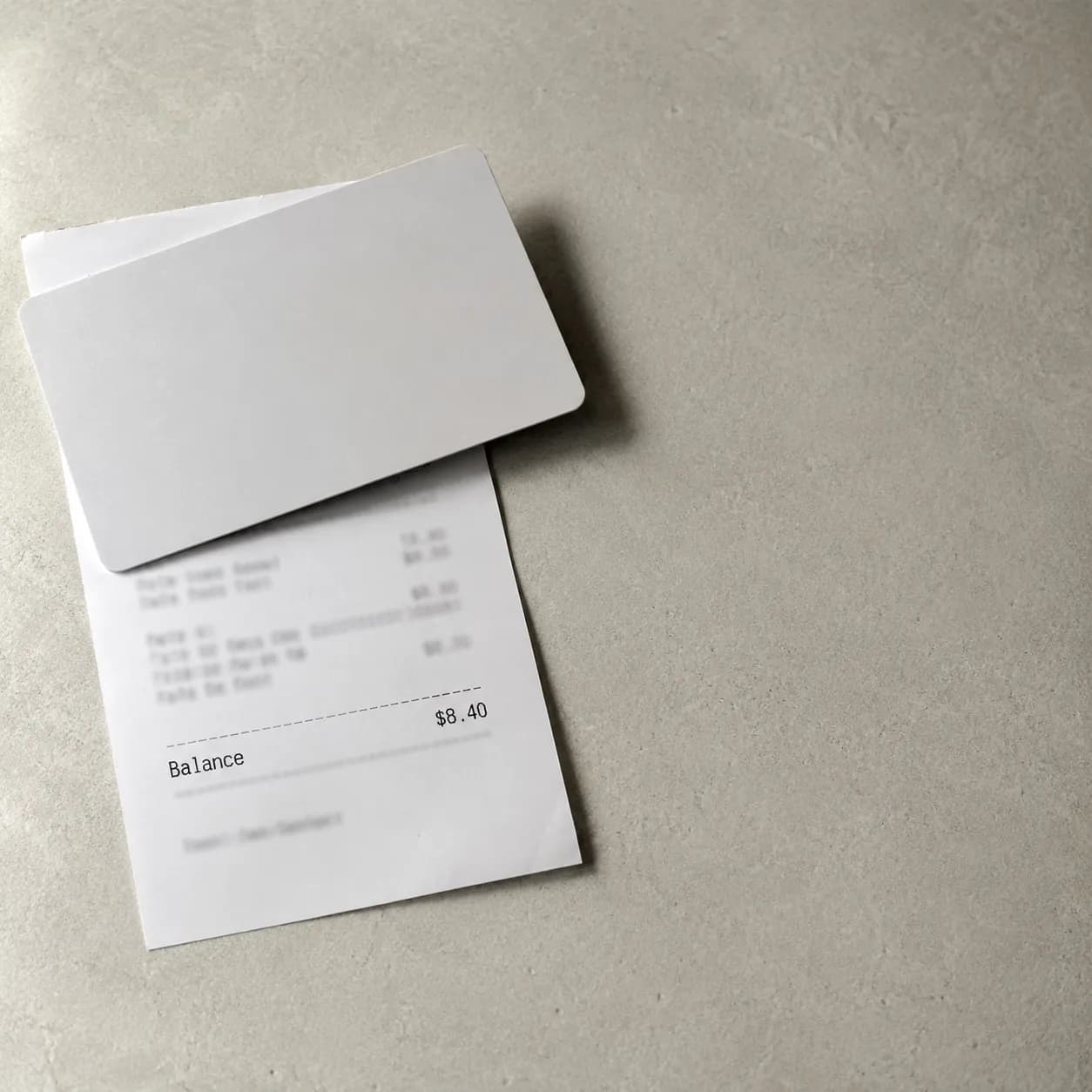 Close-up documentary-style photo of an unbranded gift card resting on a balance receipt showing a remaining balance of $8.40, with all other receipt details obscured.