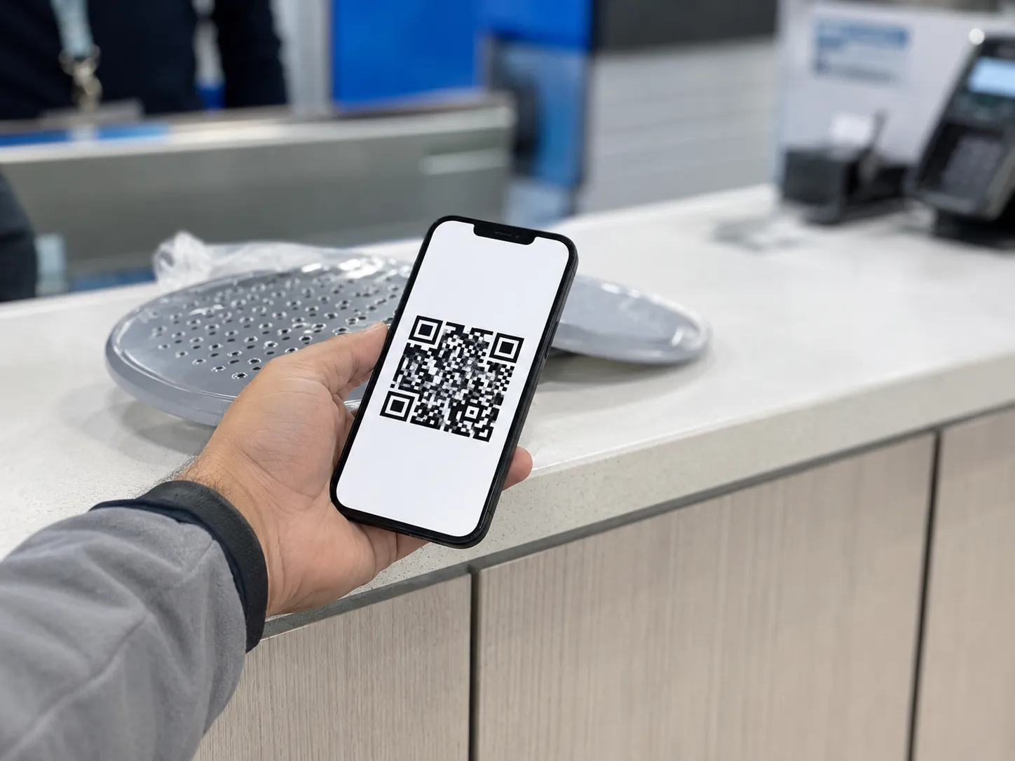 Hand holding a smartphone displaying a return barcode at a retail service desk, with an unpackaged household item on the counter during a return in Round Rock, April 2026.