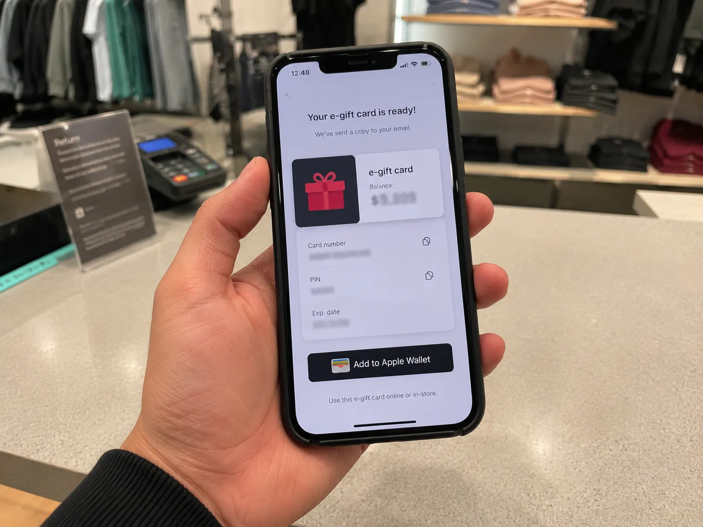 Smartphone showing a Lululemon e-gift card issued for a member sale-item return, held above a store counter