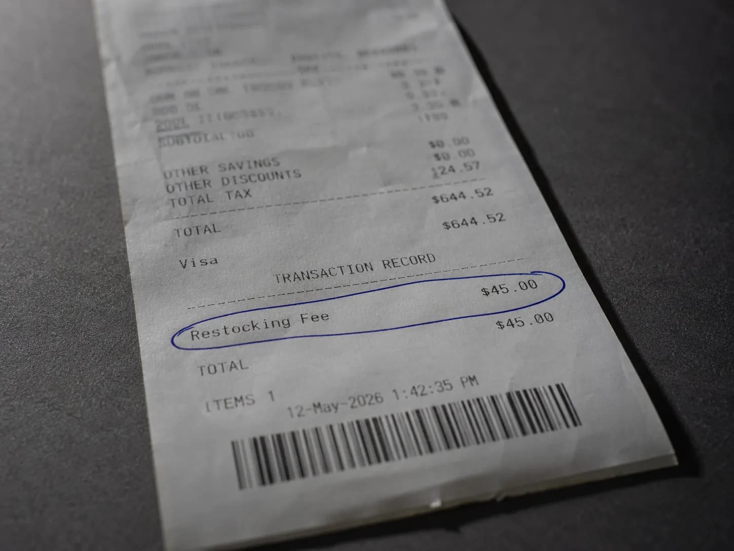 Close-up of a retail receipt showing a $45 restocking fee highlighted with a blue circle on a dark counter, Ontario, dated May 12, 2026.