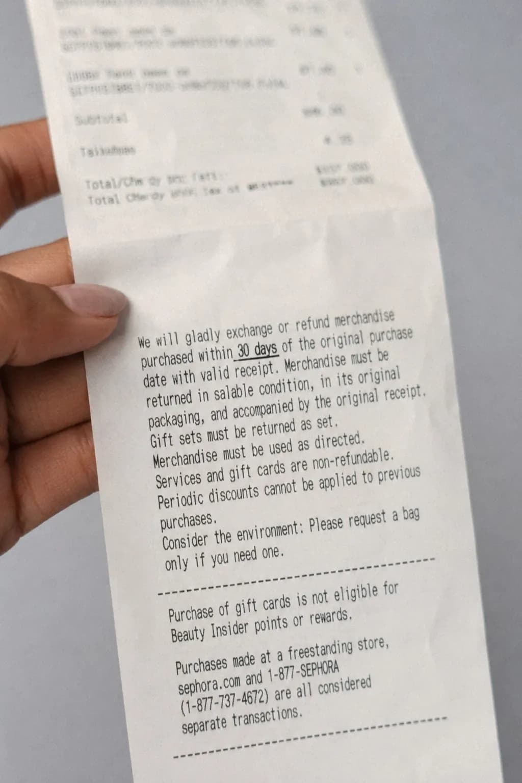 Close-up of the back of a retail receipt showing return policy fine print with 30-day return language in focus, held at a slight angle under even indoor lighting.