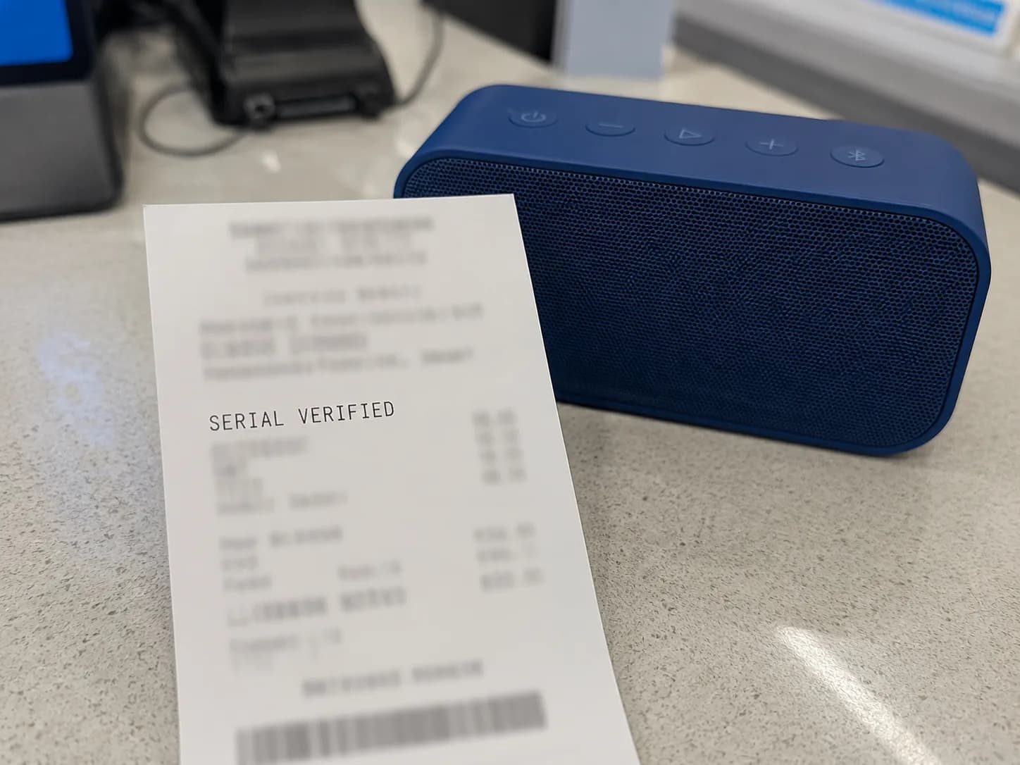 Return receipt beside a portable speaker showing “SERIAL VERIFIED,” with the serial number and other identifying details blurred during an electronics return verification.