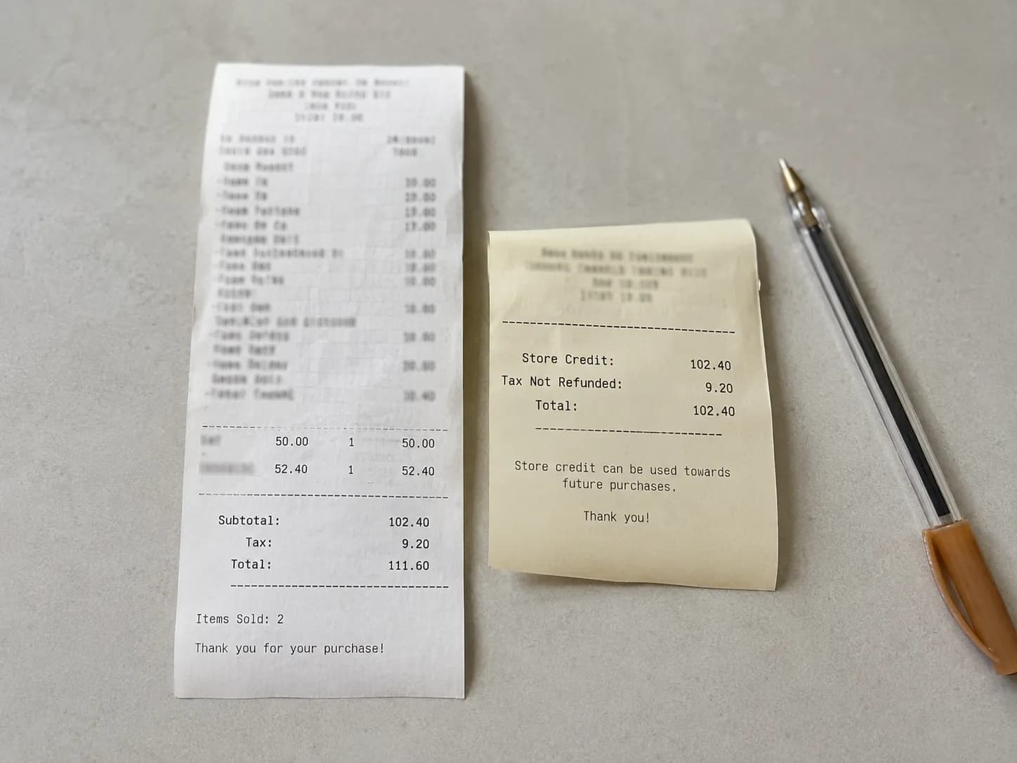 Overhead photo of a store credit slip beside an original purchase receipt, highlighting that tax was not refunded, with a ballpoint pen on a light gray surface