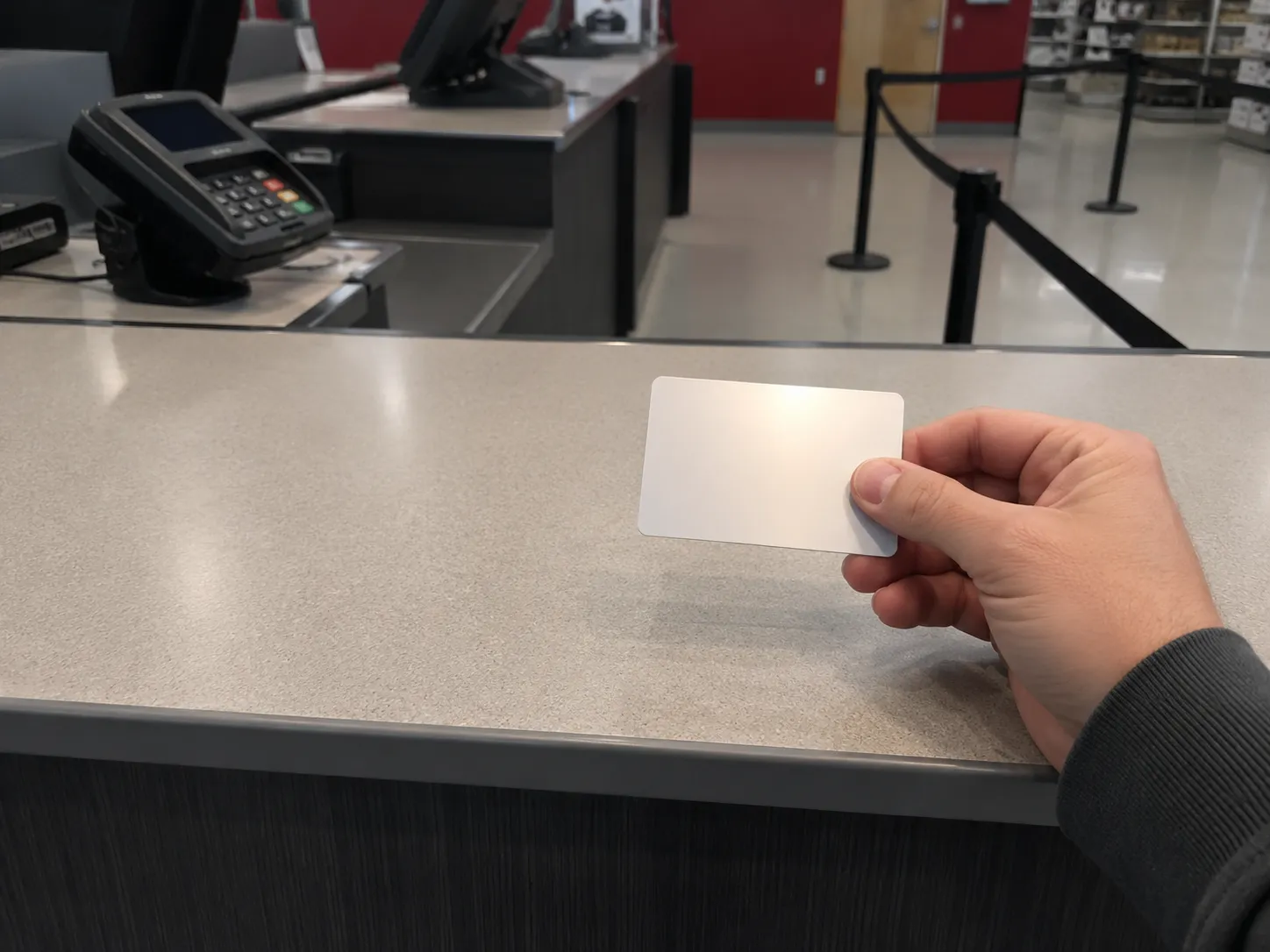 Representative illustration of an unopened $25 test gift card held over a retail Guest Services counter with a card payment terminal and queue barrier in the background, no faces, logos, or readable.