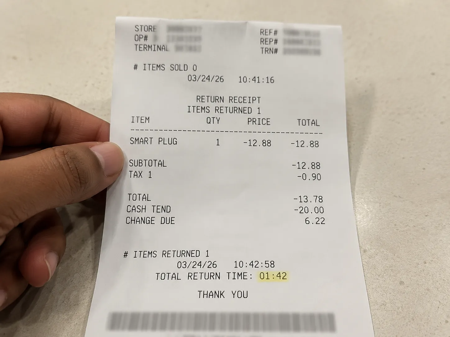 Overhead view of a return receipt for a smart plug, held by one hand, with the transaction completed in under two minutes and personal details removed.
